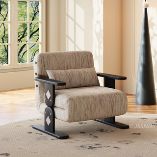 A modern beige textured armchair sits centered on a patterned area rug in a sunlit room. The chair features distinct dark wooden legs and flat armrests with decorative diamond inlay accents on the side supports. A matching elongated lumbar pillow rests against its cushioned backrest. In the background, a large window reveals green foliage alongside a unique dark cone-shaped floor lamp.