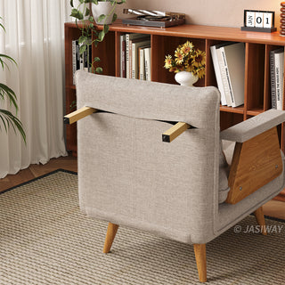 A rear view of the beige tufted fabric convertible armchair shows its wooden legs and distinctive wooden side panels. Two support legs are neatly stored and partially visible within a zippered compartment on the backrest. In the background, a warm wooden bookcase filled with books and a vase of flowers completes the cozy room setup.