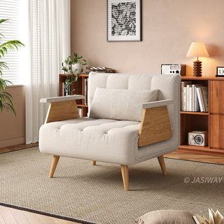A modern convertible armchair upholstered in textured beige fabric sits on a neutral area rug over a wooden floor. The armchair features button-tufting on the seat and back cushions, matching armrest pads, wooden armrest panels, and tapered wooden legs. In the background, a cozy living room with a warm tan wall, a wooden bookshelf filled with books, and a table lamp creates a warm and inviting atmosphere.