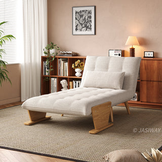 A modern convertible chaise lounge upholstered in textured beige fabric is set up as a recliner on a neutral area rug over a wooden floor. The lounge features button-tufting on the seat and back cushions, a matching rectangular lumbar pillow, wooden side panel accents, and low wooden block-style legs. In the background, a cozy room with a warm tan wall, a wooden bookshelf filled with books, and a table lamp creates a warm and inviting atmosphere.