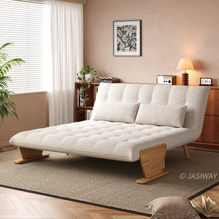 A beige tufted fabric convertible sofa is set up as a lounge chaise on a textured area rug in a sunlit room. Two matching rectangular lumbar pillows rest against its reclined backrest. In the background, a warm wooden cabinet, a table lamp, and framed wall art complete the cozy interior.