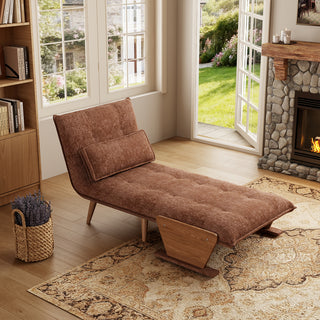 A rust-brown tufted fabric convertible sofa is set up as a lounge chaise on a patterned area rug in a sunlit room. A matching rectangular lumbar pillow rests against its reclined backrest. In the background, open glass doors reveal a green garden view next to a warm stone fireplace, completing the inviting interior.