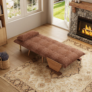 A fully flattened rust-brown tufted fabric convertible sofa bed rests on a patterned area rug in a cozy living room. A matching pillow is positioned neatly at the head of the bed. In the background, open glass doors reveal a green garden view next to a warm stone fireplace, completing the inviting interior.