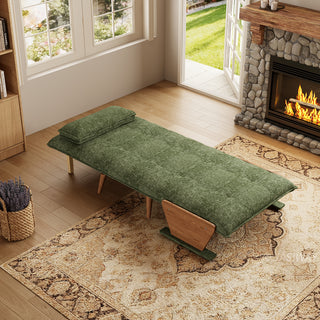 A modern convertible daybed fully extended into a flat sleeping position is upholstered in textured green fabric and rests on a patterned area rug over a wooden floor. The mattress surface features neat button-tufting, complemented by a matching bolster pillow and wooden side panel supports. In the background, a cozy room setting with a warm stone fireplace, a wooden mantel, and a window with natural daylight creates a warm, inviting atmosphere.