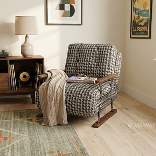A black and white houndstooth pattern convertible sleeper sofa armchair featuring metal and wood-trimmed arms, draped with a cream cable-knit throw blanket, in a California-style living room with a vintage media console, a table lamp, and framed art.