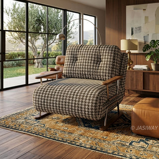 A brown and white houndstooth pattern convertible sleeper sofa armchair featuring metal and wood-trimmed arms in a modern living room with large grid windows overlooking a scenic outdoor landscape, an arched floor lamp, a patterned area rug, and a console table with a lamp.