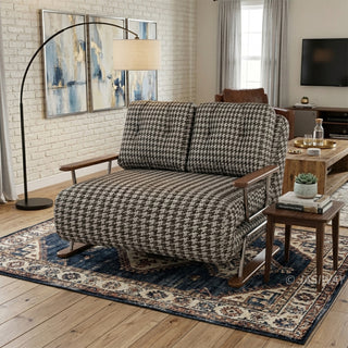A brown and white houndstooth pattern convertible sleeper sofa loveseat featuring metal and wood-trimmed arms in a contemporary living room with a white brick accent wall, an arched floor lamp, abstract wall art, and a patterned blue area rug.