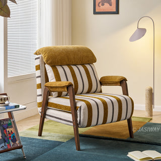 A yellow-and-white striped convertible armchair sits on a colorful multi-toned rug in a bright, modern room. A matching striped lumbar pillow and a plush headrest cushion rest against its back, framed by dark wooden armrests and legs. In the background, a large window with blinds, a modern floor lamp, and a small side table complete the cozy interior setup.