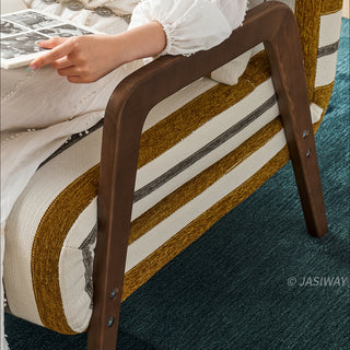 A close-up shot focuses on the dark wooden armrest and sturdy angled leg of a yellow-and-white striped convertible armchair. A person wearing a white dress sits in the chair, holding an open magazine. The textured fabric upholstery of the seat highlights the pattern clearly. The chair is positioned over a rich blue carpet.