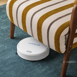 A white robotic vacuum cleaner is shown cleaning underneath a yellow-and-white striped convertible armchair. The compact vacuum fits easily into the clearance space beneath the chair's dark wooden legs. The armchair features textured fabric upholstery and rests on a deep blue textured rug.