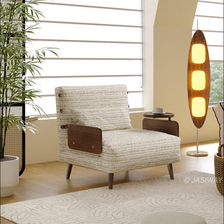 A light neutral-toned textured fabric armchair with dark wooden armrests and legs sits on a patterned rug in a bright, modern room. A sleek, tall wooden floor lamp with three glowing panels stands to the right, and a potted plant adds a touch of green on the left. The space is filled with soft natural light coming through horizontal blinds on the window behind the chair.