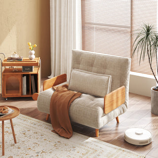 A beige linen convertible armchair features wooden armrests, tapered legs, and a matching rectangular lumbar pillow against a sunlit room setting. A warm brown throw blanket is draped neatly across the seat, adding a cozy touch. Nearby, a patterned rug, a wooden side cart with flowers, and a robotic vacuum complete the inviting living space.