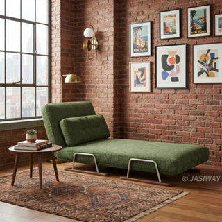 A modern daybed upholstered in textured green fabric is set up in an industrial loft with exposed brick walls. The daybed features a supportive back cushion, a sleek sled base, and rests on a patterned rug over hardwood flooring. A small wooden side table sits beside it, while a large grid window and a gallery wall of framed prints complete the urban aesthetic.