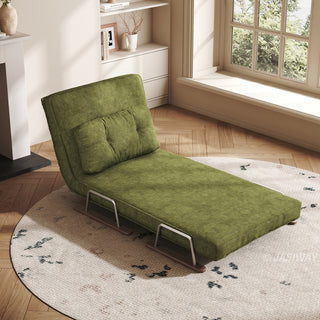 A green textured fabric convertible sofa is shown in a partially reclined chaise lounge configuration, resting on a round patterned rug. The backrest is propped up at an angle with a matching tufted bolster pillow placed against it. The warm, sunlit room features a herringbone wood floor, a window with natural light, and a minimalist bookshelf in the background.