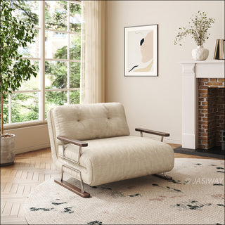 A modern, bright living room features a beige textured fabric armchair sofa with dark wood armrests and metal frame, placed centrally on a patterned round rug. In the background, a large window with sheer curtains allows natural light to flood the wooden-floored space. To the right, a brick fireplace mantle decorated with a vase and framed abstract art completes the cozy, elegant interior decor.