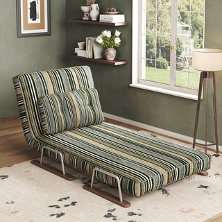 A modern convertible chaise lounge upholstered in dark striped fabric with green, black, and beige tones is set up in a corner living space on a patterned area rug over a wooden floor. The lounge features an adjustable backrest, a matching lumbar pillow, and a sleek sled base. In the background, an olive-green wall with floating shelves, a window with natural light, and a standing floor lamp completes the cozy, eclectic decor.