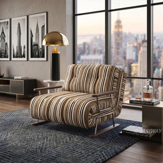A modern armchair upholstered in warm brown, black, and beige striped fabric sits on a textured dark blue area rug over a wooden floor. The chair features button-tufted back cushions, wooden armrests, and a sleek sled base. In the background, a luxury high-rise apartment with a sweeping city skyline view through large windows, black-and-white city photography, a modern gold lamp, and a sleek side table complete the sophisticated urban setting.