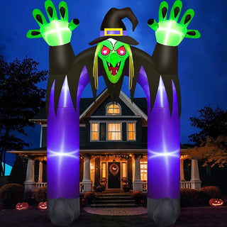Giant Halloween inflatable witch gateway and spooky archway yard decoration featuring glowing green hands, witch hat, red LED eyes, and purple pillars displayed in front of a suburban house at night.