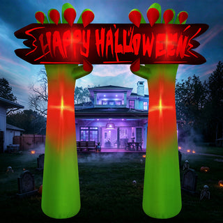 Nighttime outdoor display of a giant Halloween inflatable arch yard decoration featuring green zombie hands holding a glowing "Happy Halloween" sign on a lawn in front of a house.