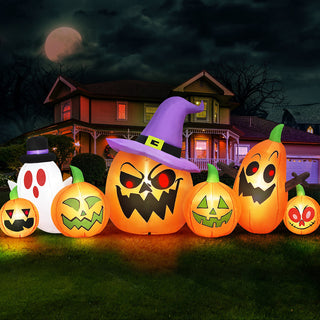 Nighttime outdoor display of a group of Halloween inflatable decorations featuring illuminated jack-o-lantern pumpkins, a witch hat pumpkin, and a ghost on a lawn in front of a house.