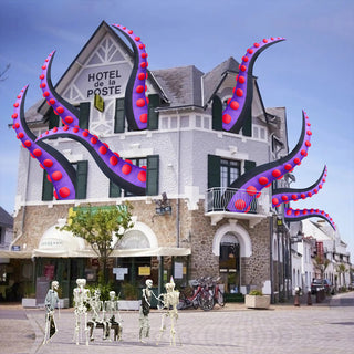 Giant Halloween inflatable purple and black monster tentacle yard decorations bursting out of the windows and roof of a classic European hotel building for an epic commercial and residential Halloween holiday display.