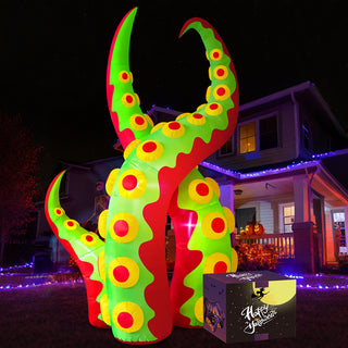 Nighttime outdoor display of a giant Halloween inflatable green and red monster tentacle yard decoration with yellow suckers, shown with its product packaging box on a lawn in front of a residential house.