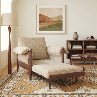 Lifestyle staging shot of a beige accent armchair with a matching ottoman, dark wood frame, and plush cushions in a warm, patterned living room.