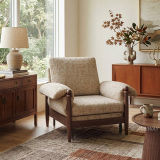 Lifestyle staging shot of a beige textured fabric accent armchair with dark wood framing in a sunlit living room.