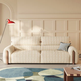 Modern cream and beige textured houndstooth tweed fabric sofa with walnut wood side accents and a black and white plaid throw pillow, set against a wainscoted wall on a colorful geometric rug.