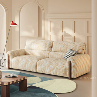 Modern cream and beige textured houndstooth tweed fabric sofa with walnut wood side accents, styled in an elegant room with arched alcoves, a red floor lamp, and a geometric area rug.