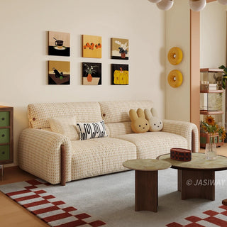 Modern cream and beige houndstooth tweed fabric sofa styled with cute bunny cushions and a patterned throw pillow, featuring framed artwork on the wall and round coffee tables in a cozy living room setting.