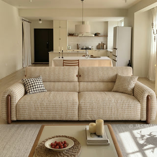 Front view of a modern cream and beige houndstooth tweed fabric sofa with walnut wood side accents, styled with a black and white grid throw pillow in a spacious open-concept living room and kitchen setup.