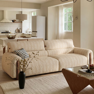 Three-quarter angle view of a modern cream and beige houndstooth tweed sofa with walnut wood trim accents, styled in an open-concept living room featuring an adjacent dining area and bright window lighting.