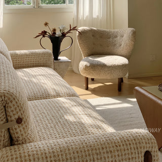 Close-up side view of a cream houndstooth tweed sofa with a plush ivory bouclé accent armchair in a sunlit corner of a modern living room.