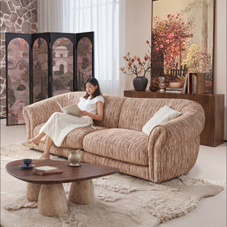 JASIWAY luxury curved chenille sofa featuring a structural biomorphic design, deep seat cushions, and premium textured multi-tonal chenille upholstery. This modern cloud couch showcases tailored rolled arms with integrated piping details and an organic, gently arched back silhouette.-Three quarter view with model sitting