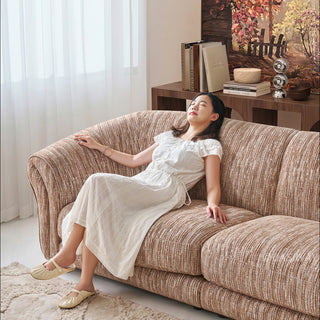 JASIWAY luxury curved chenille sofa featuring a structural biomorphic design, deep seat cushions, and premium textured multi-tonal chenille upholstery. This modern cloud couch showcases tailored rolled arms with integrated piping details and an organic, gently arched back silhouette.-Medium shot with model reclining