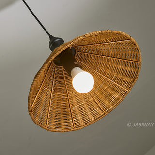 This is an upward-angle photograph of a pendant lamp featuring a conical, woven rattan shade. The textured natural fibers are densely woven around an internal frame, suspended by a black cord and fixture. A single lit LED bulb is centered within the shade, casting a bright glow against the neutral background.