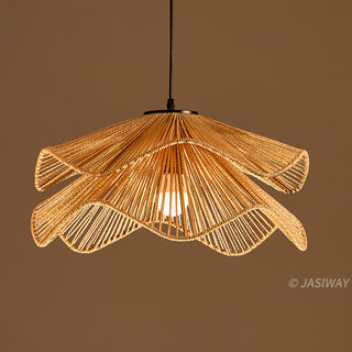 A pendant light fixture crafted from tightly woven, light-brown natural fibers hangs against a warm brown background. The intricate lampshade features an undulating, two-tiered design that resembles the overlapping wavy petals of a flower. A sleek black cord suspends the fixture, revealing a single illuminated white bulb radiating light through the gaps in the woven strands.