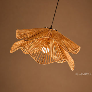 A pendant light fixture made of tightly woven, natural light-brown fibers hangs against a warm brown background. Its intricate, two-tiered lampshade features an undulating, floral-inspired design that allows light from a single central bulb to shine through. Suspended by a thin cord, the lamp creates a soft, ambient glow.