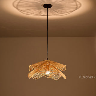 A pendant light fixture, crafted from woven, light-brown natural fibers, hangs centered against a warm brown background. The two-tiered lampshade features an intricate, undulating design resembling a blooming flower, with the strands radiating outward from the center. A single illuminated bulb is visible within the woven structure, casting light and creating a soft shadow pattern on the ceiling above.