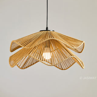 A pendant light fixture made of tightly woven, natural light-brown fibers hangs against a neutral, light-grey background. The intricate lampshade features a unique two-tiered, wavy design that mimics the petals of a blooming flower. A sleek black cord suspends the lamp, with a single glowing white bulb visible inside the structure.