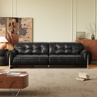 A sleek, black leather sofa with button-tufted back cushions as the focal point of a sophisticated living room. The sofa is positioned in front of an ornate folding screen and beside a wooden cabinet, with a coffee table and an open book placed on the rug in the foreground. The elegant space is completed by soft lighting and a minimalist aesthetic.