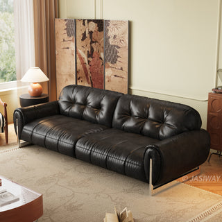 A sophisticated black leather sofa with a plush, button-tufted backrest and a sleek, paneled seat design. It is supported by minimalist chrome legs, giving it a contemporary look. The sofa is the centerpiece of a warmly lit living room, placed on a textured rug with a wooden cabinet and an ornate folding screen in the background.
