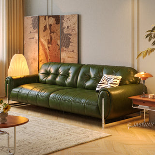 A luxurious deep green leather sofa, highlighted by button-tufted back cushions and sleek chrome legs. The sofa is accented with a zebra-print throw pillow and placed within a stylishly appointed room featuring a patterned area rug, an ornate folding screen, and warm accent lighting. A side table and modern decor complete the sophisticated look.