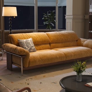 JASIWAY mid-century modern 3-seater sofa featuring textured chenille upholstery, sculptural curved armrests with integrated solid wood supports, and a low-profile exposed timber base frame accented by slender polished metal legs.-Three-quarter view at night