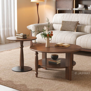JASIWAY mid-century modern round coffee table set crafted from rich walnut-finished solid wood, a lower open storage shelf holding books, and an architectural leg design with elegant turned wood detailing. The tall, slim accent end table showcases a matching round wooden top supported by a sculptural pedestal base with a dark metal floor plate, styled alongside a warm contemporary living room sofa.-Three quarter view