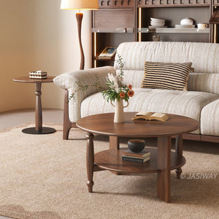JASIWAY mid-century modern round coffee table set crafted from rich walnut-finished solid wood, a lower open storage shelf holding books, and an architectural leg design with elegant turned wood detailing. The tall, slim accent end table showcases a matching round wooden top supported by a sculptural pedestal base with a dark metal floor plate, styled alongside a warm contemporary living room sofa.-Diagonal view