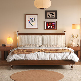A mid-century modern bedroom featuring a wooden bed frame with a textured striped headboard, accented by two wooden nightstands, warm ambient lighting from bedside lamps and a paper pendant light, and three abstract art pieces displayed on the wall above the bed.