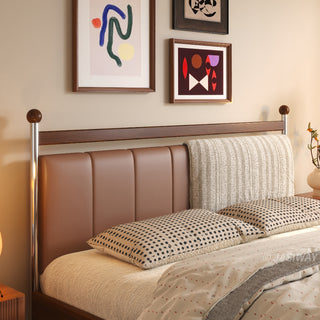 A close-up view of a mid-century modern solid wood bed frame, showcasing a unique, split-design headboard that features one side in sleek, channel-tufted leather and the other in a textured, woven fabric, positioned beneath framed abstract art.