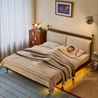 A high-angle view of a model sleeping soundly in a mid-century modern solid wood platform bed, which features a textured upholstered headboard and integrated, warm under-bed LED lighting that illuminates the surrounding grid-patterned rug.